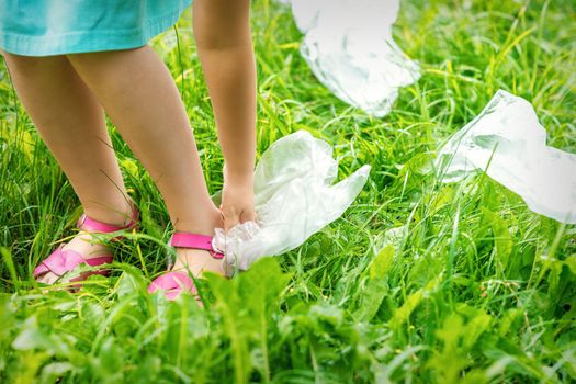Little girl cleans plastic bags on the green grass in the park