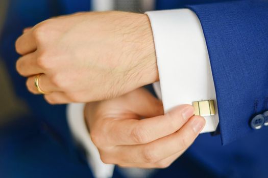 Groom or businessman fasten cufflink on the cuff of the shirt wearing blue suit. Blurred
