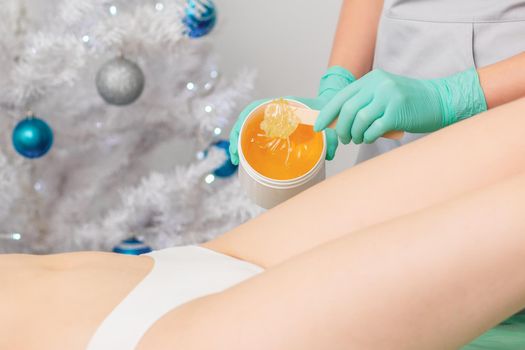 Young woman getting wax epilation of legs. Depilation concept. Product waxing bowl. Christmas discount waxing