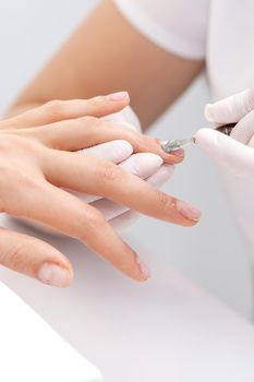 Hands of manicurist pushing cuticles on female's nails with manicure tool. Woman receiving manicure and nail care procedure