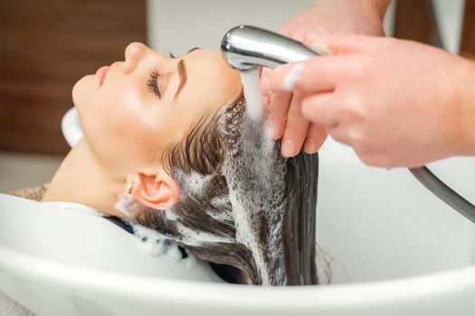 Close up of hands of hairdresser washing hair of woman in sink at beauty salon