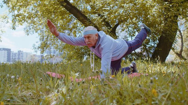 Fitness for seniors. Elderly man exercising at park making yoga stretching exercise, practicing sports training on green grass. Active retired mature old people. Grandfather enjoying healthy lifestyle