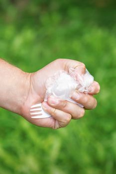 Close up of hand of man holding plastic utensils trash on a background of green grass in the park