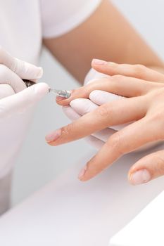 Hands of manicurist pushing cuticles on female's nails with manicure tool. Woman receiving manicure and nail care procedure