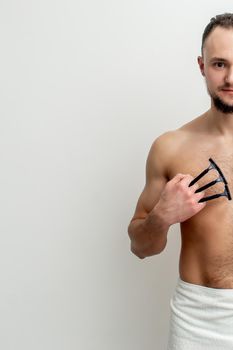 Young caucasian man with beard holds razor shaves his chest with white shaving foam on white background. Man shaving his torso