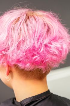 Pink hairstyle of young woman after coloring hair with highlights in beauty salon