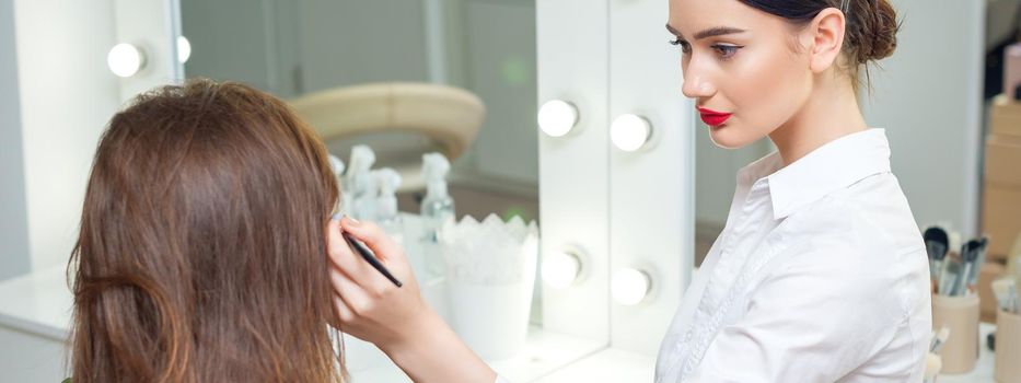 Makeup artist working with her client near the mirror in the beauty salon