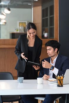 Beautiful businewoman discussing project planning with colleague and giving advice on financial data report.