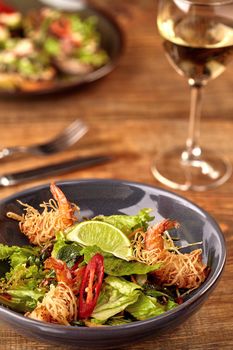 Prawn salad with lettuce and lime in bowl on wooden table. Top view. Still life