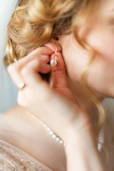 Beautiful caucasian young bride dresses earrings before wedding. Selective focus