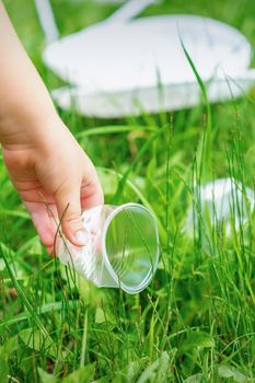 Little girl cleans plastic utensils on the green grass in the park