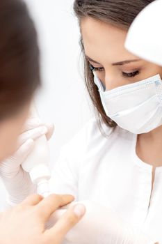 Professional manicurist with protective mask pouring oil on nails manicure of woman in beauty salon.