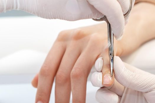 Close up of manicurist using manicure scissors to remove cuticle of female nails in manicure salon