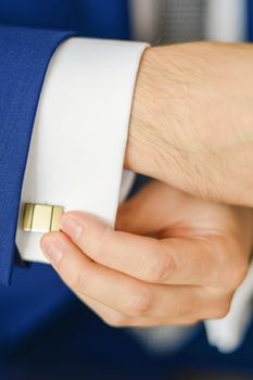 Groom or businessman fasten cufflink on the cuff of the shirt wearing blue suit. Soft focus
