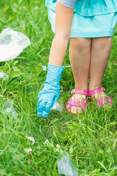 Little girl cleans plastic trash on the green grass in the park