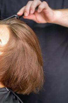 Hand of hairdresser combs hair of young caucasian woman in beauty salon.