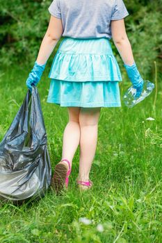 Little girl cleans plastic trash on the green grass in the park