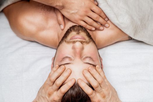 Top view of man receiving relaxing head massage by hands of massage therapist