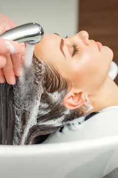 Close up of hands of hairdresser washing hair of woman in sink at beauty salon