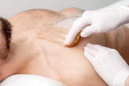 Epilation chest of young male with liquid wax paste by hands of female cosmetologist in beauty salon