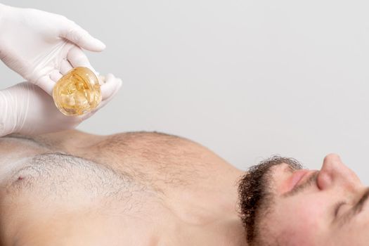 Epilation chest of young male with liquid wax paste by hands of female cosmetologist in beauty salon