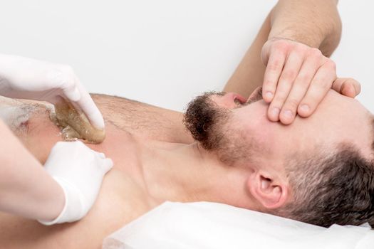 Epilation chest of young male with liquid wax paste by hands of female cosmetologist in beauty salon