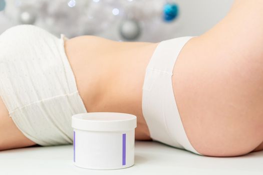 Cosmetics white jar near lying woman body on christmass tree background. Concept of New Year discounts
