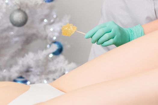 Young woman getting wax epilation of legs. Depilation concept. Product waxing bowl. Christmas discount waxing