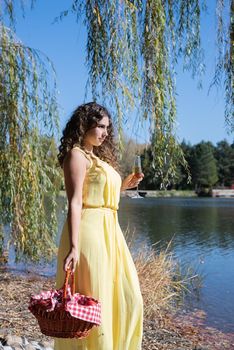 Leisure, free time. Beautiful caucasian woman in yellow dress on a picnic outdoors, sitting next to water