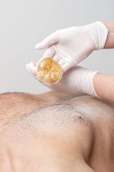 Epilation chest of young male with liquid wax paste by hands of female cosmetologist in beauty salon