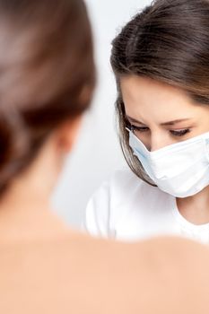 Manicurist wearing protective mask painting female nails with nail polish in manicure salon.