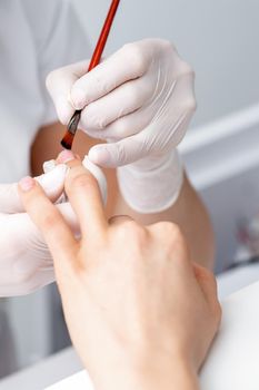 Manicure master in rubber gloves applying transparent nail polish on female nails in beauty salon