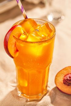 Summer cold drinks: peach sangria with ice cubes in glass on sand background. Close-up. Still life. Copy space