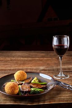 Stewed beef with vegetables and a glass of red dry wine on wooden table, close up. Hot Meat Dishes. Still life. Copy space. Flat lay. Concept restaurant menu