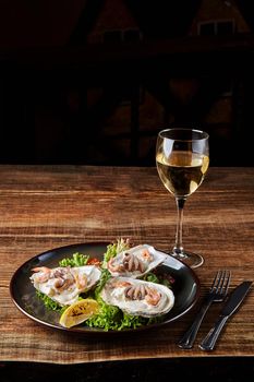 Seafood. Restaurant cuisine, healthy delicatessen food. Oysters, shrimps, octopus in white cream sauce in the shell of oysters. Original serving of ready meals. Dark plate on wooden background