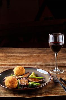 Stewed beef with vegetables and a glass of red dry wine on wooden table, close up. Hot Meat Dishes. Still life. Copy space. Flat lay. Concept restaurant menu