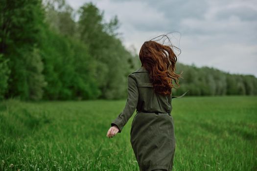 a woman in a long raincoat runs across a field in tall green grass in cloudy weather in spring. High quality photo