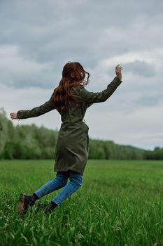 happy woman in a long raincoat jumping in a green field in cloudy weather. High quality photo