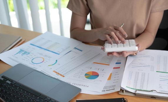 Close up of businesswoman or accountant using calculator to calculate calculate business data, working at office with paper document and laptop computer on office table, business and finance concept.