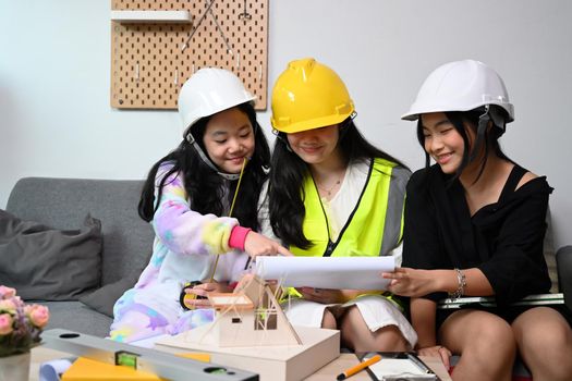 Three asian children wearing construction uniform and helmet while playing together at home.