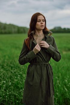 a beautiful woman stands in a green field and adjusts her coat. High quality photo