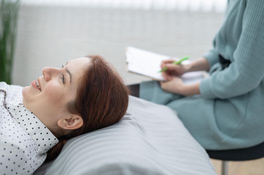 A caucasian woman lies on a couch and expresses her feelings, while a psychologist makes notes on a tablet