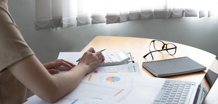 Close up of businesswoman or accountant using calculator to calculate calculate business data, working at office with paper document and laptop computer on office table, business and finance concept.