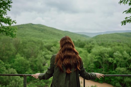 a red-haired woman with beautiful, well-groomed, long hair stands with her back to the camera and enjoys the view of the forest. High quality photo