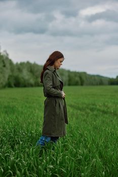 a woman in a long raincoat stands in tall green grass in a field in rainy weather in spring. High quality photo