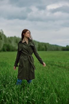 a woman in a long raincoat stands in tall green grass in a field in rainy weather in spring. High quality photo