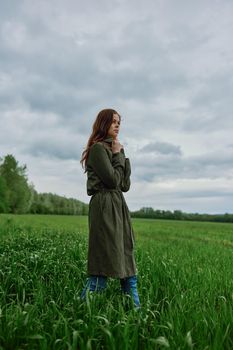 a beautiful woman in a dark coat stands in a green field in the spring in rainy weather. High quality photo