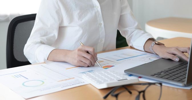 Businesswoman working at office with calculator and laptop computer calculating financial report graph data documents on desk, close up, business analysis, work process concept.