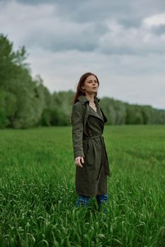 a woman in a long raincoat stands in tall green grass in a field in rainy weather in spring. High quality photo