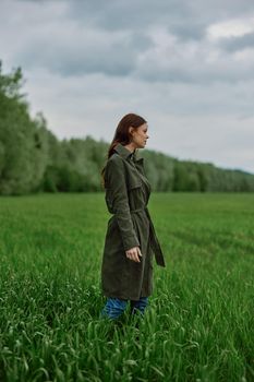 a woman in a long raincoat stands in tall green grass in a field in rainy weather in spring. High quality photo